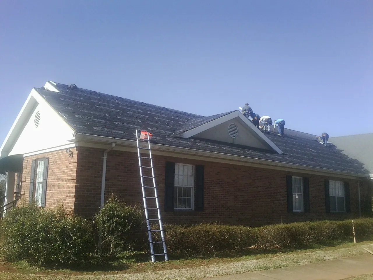 Crew tearing shingles off a brick ranch roof with a ladder set — Emergency Roof Repair work by our crew in North Bonneville