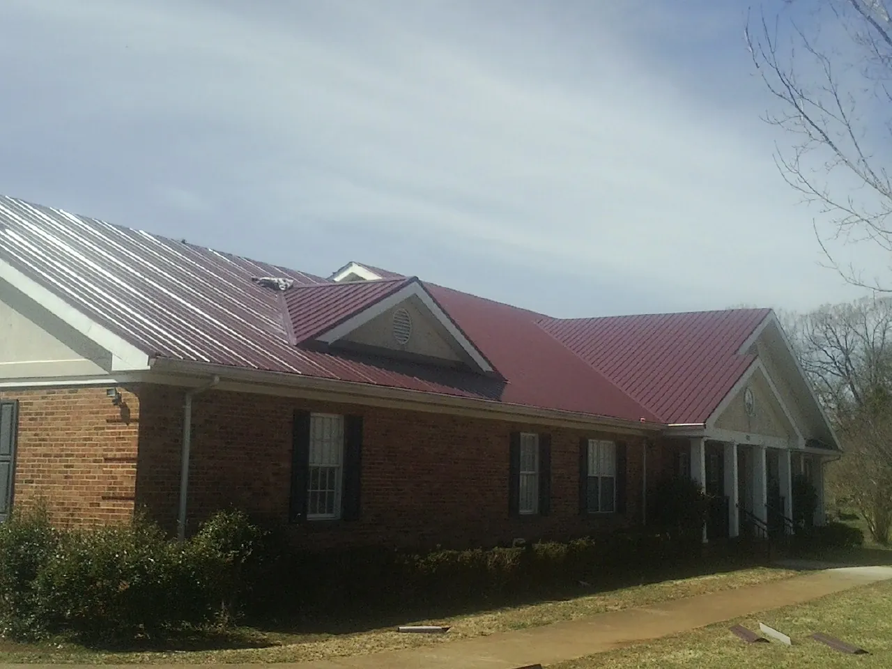 Red metal roof with gabled entries on a long brick building, from a Hail Damage Roof Repair job in North Bonneville