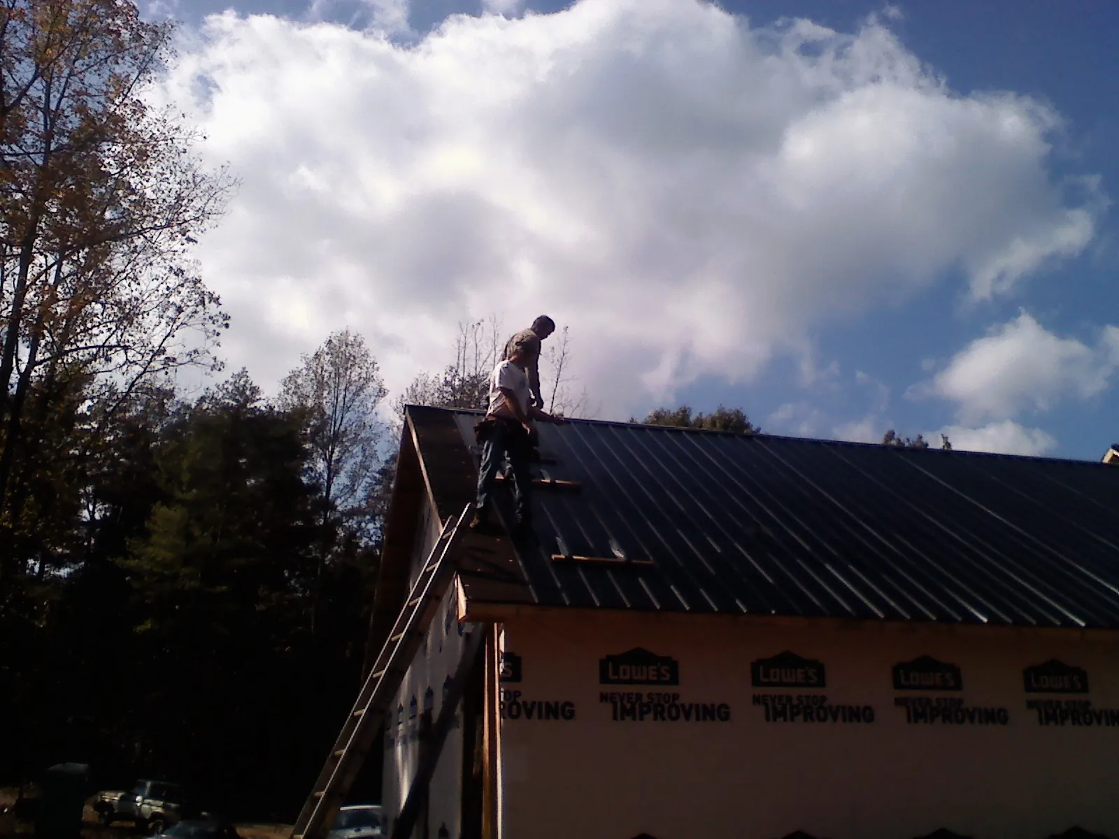 Roofer fastening dark metal panels high against a cloudy sky, from a Roof Inspection job in North Bonneville
