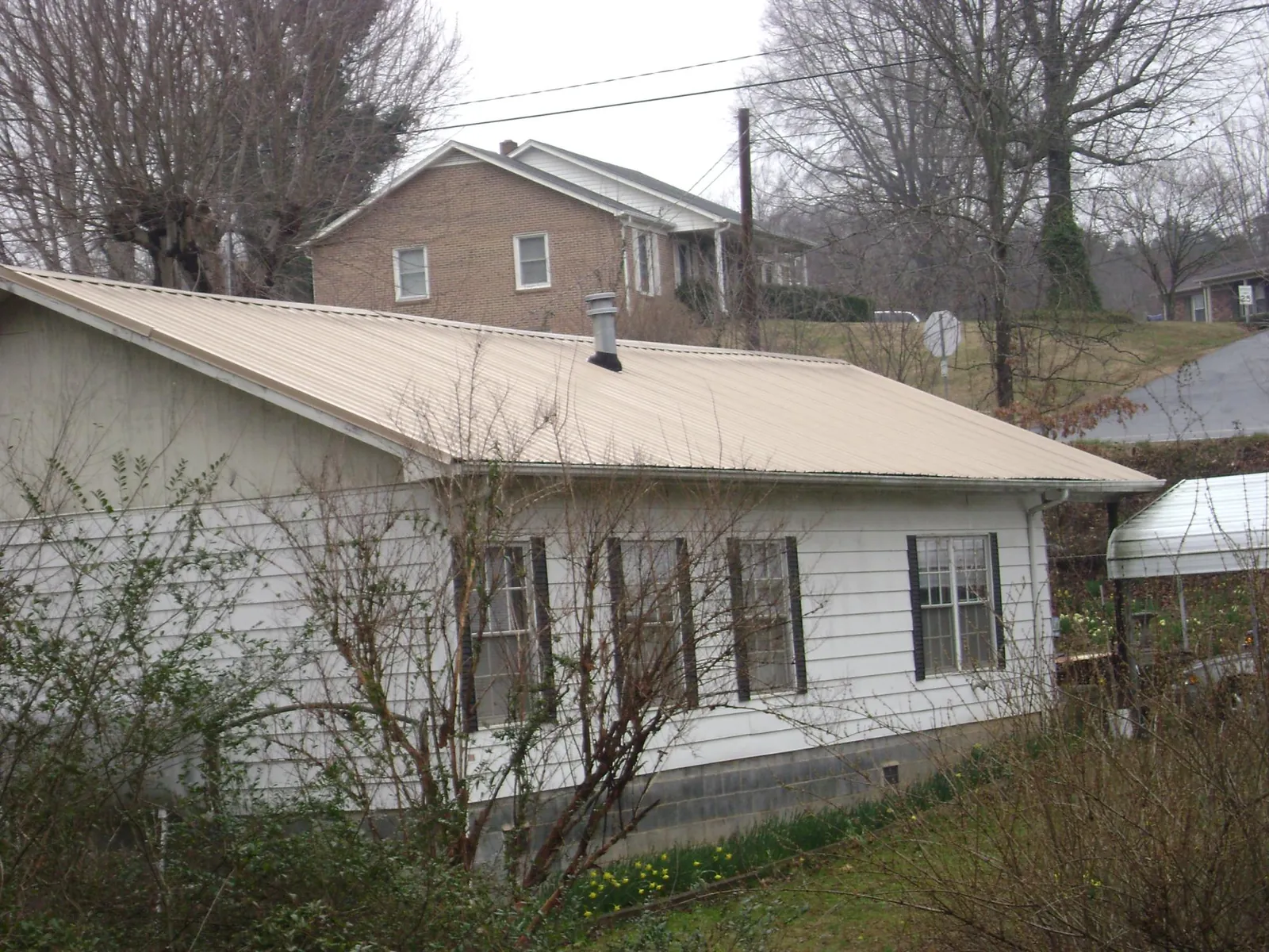 Tan metal roof on a white sided house set into a hillside — Commercial Roofing by Roofing Brothers in North Bonneville